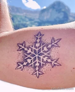 Фото тату: небольшая снежинка, выполненная в технике dotwork (точечная техника), расположена на спине. Деликатный рисунок татуировки.