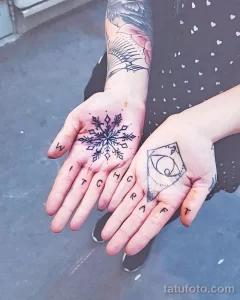 Фото тату с изображением снежинок и надписи 'Witchcraft' на ладонях. Черно-белый рисунок татуировки выполнен тонкими линиями.