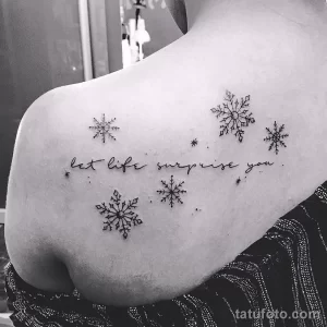 Фото тату нескольких снежинок и надписи "let life surprise you" на спине. Черно-белый рисунок с изящным дизайном и вдохновляющим текстом.