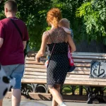 Фото тату на спине рыжеволосой женщины, гуляющей с ребенком. Рисунок татуировки выполнен в темных тонах, с преобладанием цветочных мотивов.