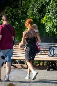 Фото тату на спине рыжеволосой женщины, гуляющей с ребенком. Рисунок татуировки выполнен в темных тонах, с преобладанием цветочных мотивов.