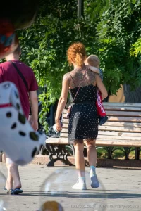 Фото тату на спине рыжеволосой женщины, гуляющей с ребенком. Рисунок татуировки выполнен в темных тонах, с преобладанием цветочных мотивов.