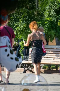 Фото тату на спине рыжеволосой женщины, гуляющей с ребенком. Рисунок татуировки выполнен в темных тонах, с преобладанием цветочных мотивов.
