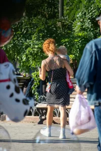 Фото тату на спине рыжеволосой женщины, гуляющей с ребенком. Рисунок татуировки выполнен в темных тонах, с преобладанием цветочных мотивов.