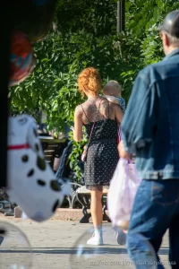Фото тату на спине рыжеволосой женщины, гуляющей с ребенком. Рисунок татуировки выполнен в темных тонах, с преобладанием цветочных мотивов.