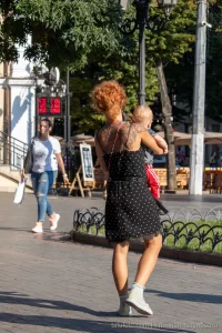 Фото тату на спине рыжеволосой женщины, гуляющей с ребенком. Рисунок татуировки выполнен в темных тонах, с преобладанием цветочных мотивов.