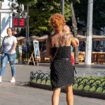 Фото тату на спине женщины, идущей по улице с ребенком. Рисунок татуировки выполнен в темных тонах, с элементами цветов и узоров.