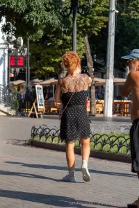 Фото тату на спине женщины с большим, красочным цветочным рисунком. Преобладают красные, розовые и зеленые оттенки, создающие эффект живых цветов.