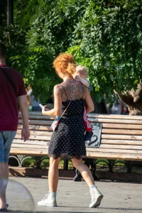 Фото тату на спине рыжеволосой женщины, гуляющей с ребенком. Рисунок татуировки выполнен в темных тонах, с преобладанием цветочных мотивов.