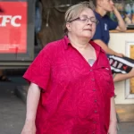 Фото женщины с татуировкой на плече, стоящей возле кафе. Уличная фотография татуировки, демонстрирующая повседневную жизнь.