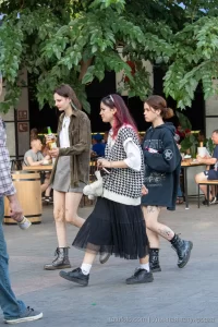 Фото трех девушек с татуировками на руках и ногах, идущих по улице. Современный стиль, уличная мода, повседневный образ, разнообразие тату.
