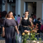 Фото тату: девушка с татуировками на руках и теле идет по городской улице, окруженная людьми и зданиями. Татуировки видны на открытой коже.
