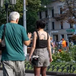 Фото тату на спине девушки, идущей по улице. Черно-белый рисунок татуировки в виде абстрактного узора, выполненный в графическом стиле.
