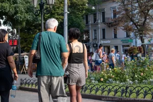 Фото тату на плече девушки, идущей по улице. Черно-белый рисунок татуировки в виде растительного орнамента, выполненный в реалистичном стиле.