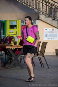 Фото тату на предплечье и голени девушки, идущей по улице. Рисунок татуировки выполнен в ярких цветах, сочетая абстрактные и флористические элементы.