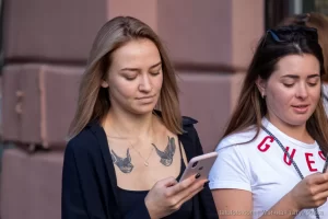 Фото крупным планом тату птиц на груди девушки, смотрящей в телефон. Рисунок татуировки выполнен в черном цвете.