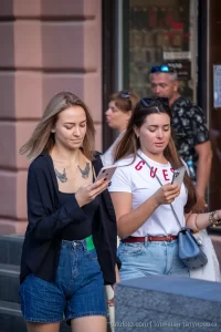 Фото девушки с тату птиц на груди, смотрящей в телефон. Рисунок татуировки выполнен в черном цвете.
