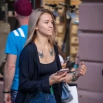 Фото тату на груди девушки, смотрящей в телефон. Рисунок татуировки изображает летящих птиц, выполненных в черном цвете.