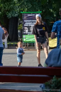 Фотография девушки с татуировкой на ноге, стоящей на улице. Девушка в шортах и футболке, с рюкзаком.