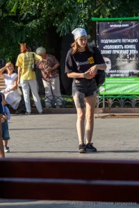Фотография девушки в повязке на голове, демонстрирующей татуировку на ноге. На заднем плане городской пейзаж и рекламный баннер.