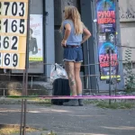 Фотография девушки с татуировкой на ноге, стоящей спиной к камере. Девушка в шортах и футболке, с рюкзаком.