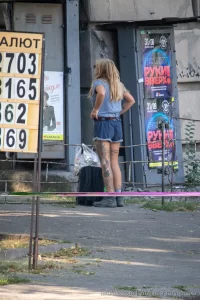 Фотография девушки с татуировкой на ноге, стоящей спиной к камере. Девушка в шортах и футболке, с рюкзаком.