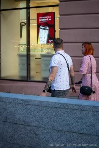 Фото тату на руке мужчины, идущего по улице. Видны детализированные рисунки на плече и предплечье, выполненные в темных тонах.