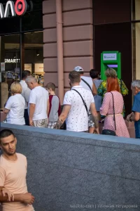 Фото мужчины с татуировкой на руке, стоящего в толпе людей. Видна часть татуировки с абстрактными узорами. Уличная фотография татуировки.