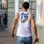 Фото татуировки на спине и руке мужчины, выполненной в различных стилях. Видны детализированные изображения и яркие цвета. Мужчина идет по улице.