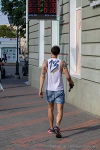 Фото татуировки на спине и руке мужчины, выполненной в различных стилях. Видны детализированные изображения и яркие цвета. Мужчина идет по улице.