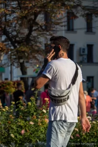 Фото тату на руке мужчины, выполненное в стиле графика. Видны детализированные изображения и темные контуры. Мужчина разговаривает по телефону на улице.