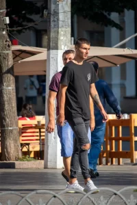 Фотография мужчины, идущего по улице, с видимой татуировкой на руке, выполненной в темных тонах.