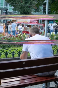 Фотография мужчины с татуировкой на плече, сидящего на скамейке в парке. Видна часть татуировки и общая атмосфера отдыха.