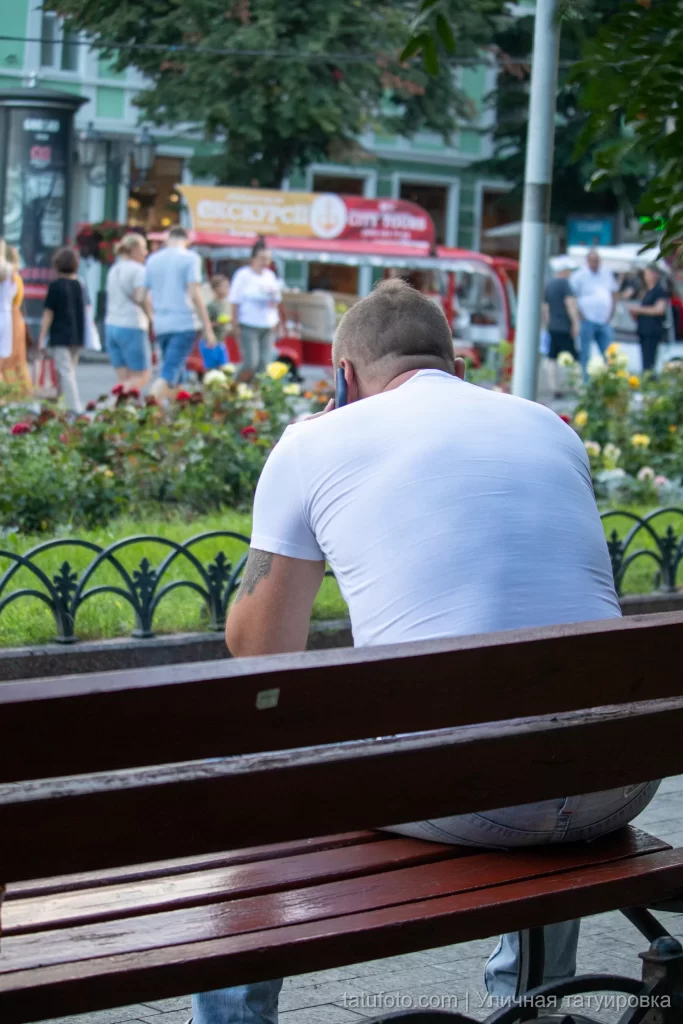 Парень с тату на плече сидит на скамейке и говорит по телефону 2 - Уличная тату (street tattoo) № 16– tatufoto.com 28082021№0469