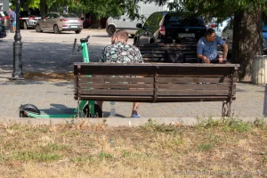 Фото тату на руке мужчины, сидящего на скамейке в парке, вид сзади, летний день, городская среда.