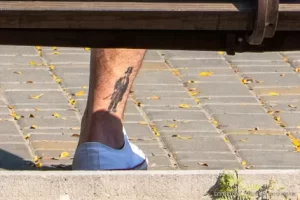 Фото тату на лодыжке мужчины, изображение джентльмена в костюме и цилиндре, выполненное в минималистичном стиле.