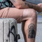 Крупный план татуировки на руке и голени мужчины. Видны детализированные рисунки в стиле графика и реализм.