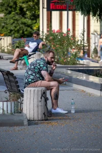 Фото тату на предплечье и голени мужчины, сидящего на улице. Видны детализированные рисунки в стиле реализм и графика.