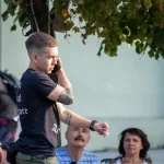Фото тату на руке мужчины, вид сбоку, он разговаривает по телефону на улице, летний день, городская среда.