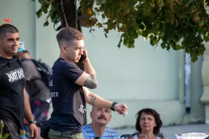Фото тату на руке мужчины, вид сбоку, он разговаривает по телефону на улице, летний день, городская среда.