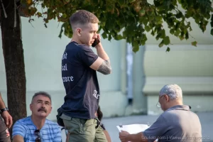 Фото тату на руке мужчины, вид сбоку, он разговаривает по телефону на улице, летний день, городская среда.