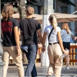 Фотография трех людей, идущих по улице. У одного из них видна татуировка на плече, у другого - на предплечье. Снимок сделан в солнечный день.