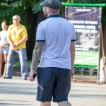 Фото мужчины в кепке с татуировкой на предплечье в стиле blackwork. Мужчина стоит спиной к камере, держа в руке телефон.