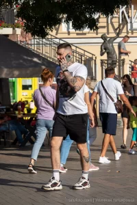 Фото мужчины с татуировками на руках и шее, разговаривающего по телефону на улице. Видны детализированные рисунки и общий вид татуировок.
