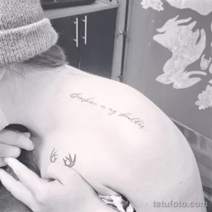 Черно-белое фото татуировки с надписью 'Sunshine on my shoulder' на женском плече. Текст выполнен изящным шрифтом, под ним небольшой рисунок.