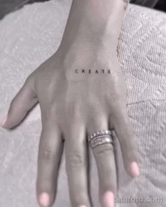 Минималистичная татуировка надписью 'CREATE' на запястье, выполненная тонкими черными буквами. Татуировка выглядит стильно и лаконично.