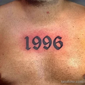 Фото тату с цифрами '1996' на груди, выполненное в простом, лаконичном стиле черными чернилами. Идеально для тех, кто ценит минимализм.