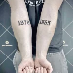 Фото татуировки на запястьях мужчины: годы рождения, выполненные в готическом стиле. Простая и символичная татуировка.