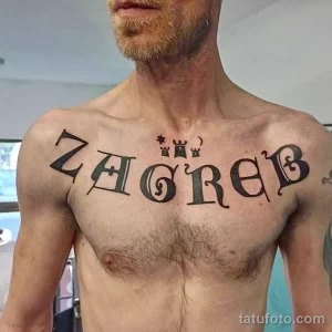 Фото тату на мужской груди: надпись "ZAGREB" в стилизованном шрифте с добавлением символов.