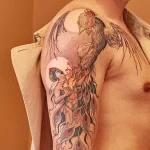 Фото тату на плече с изображением феникса, взлетающего над девушкой. Цветная татуировка с детальной проработкой перьев и лица. Эскиз тату.